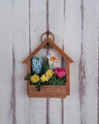 Porta fiori a forma di casetta con al suo interno un narciso, un giacinto, un crocus e dei fiori di tarassaco