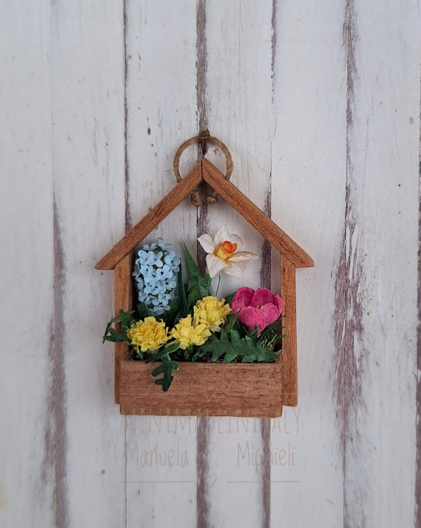 Porta fiori a forma di casetta con al suo interno un narciso, un giacinto, un crocus e dei fiori di tarassaco